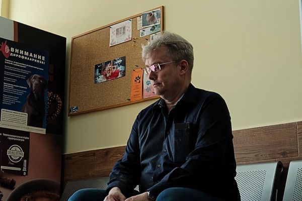 Ein Mann wartet mit seinem Hund im Wartezimmer auf de n Tierarzt